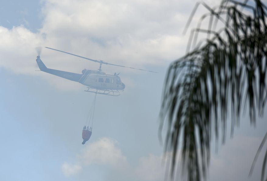 A Florida Forest Service helicopter carries a bucket through smoke while dropping water on the Silver Palm fire in the Suncoast Lakes subdivision Tuesday, April 11, 2017, in Land O' Lakes. The Silver Palm Fire burned close to homes in the Suncoast Lakes subdivision Tuesday forcing residents to use garden hoses on vegetation and roofs around their property. (Chris Urso/The Tampa Bay Times via AP)