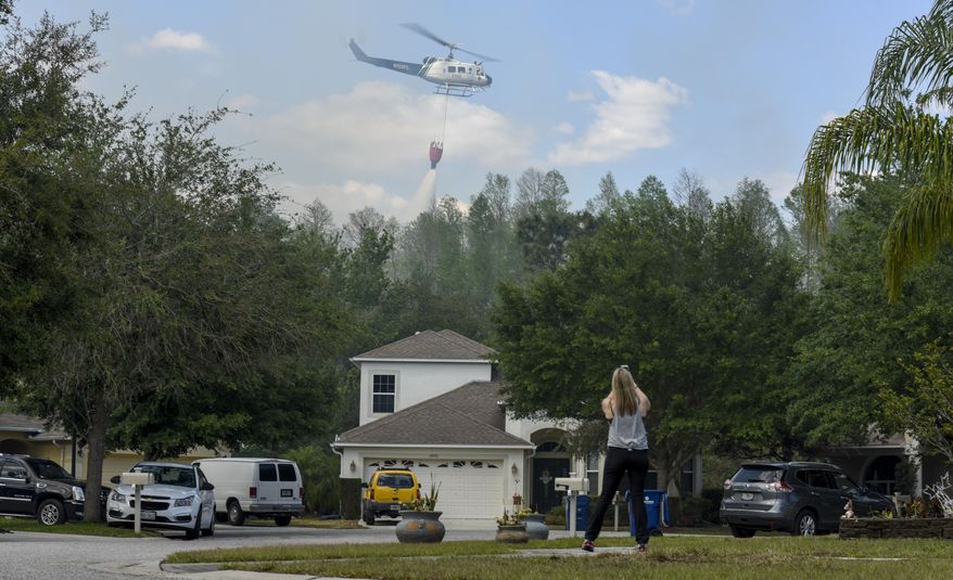 Suncoast Lakes resident Kristin Werner uses her cellphone to record a Florida Forest Service helicopter dropping water behind homes on the Silver Palm fire Tuesday, April 11, 2017, in Land O' Lakes. The Silver Palm Fire burned close to homes in the Suncoast Lakes subdivision Tuesday forcing residents to use garden hoses on vegetation and roofs around their property. (Chris Urso/The Tampa Bay Times via AP)
