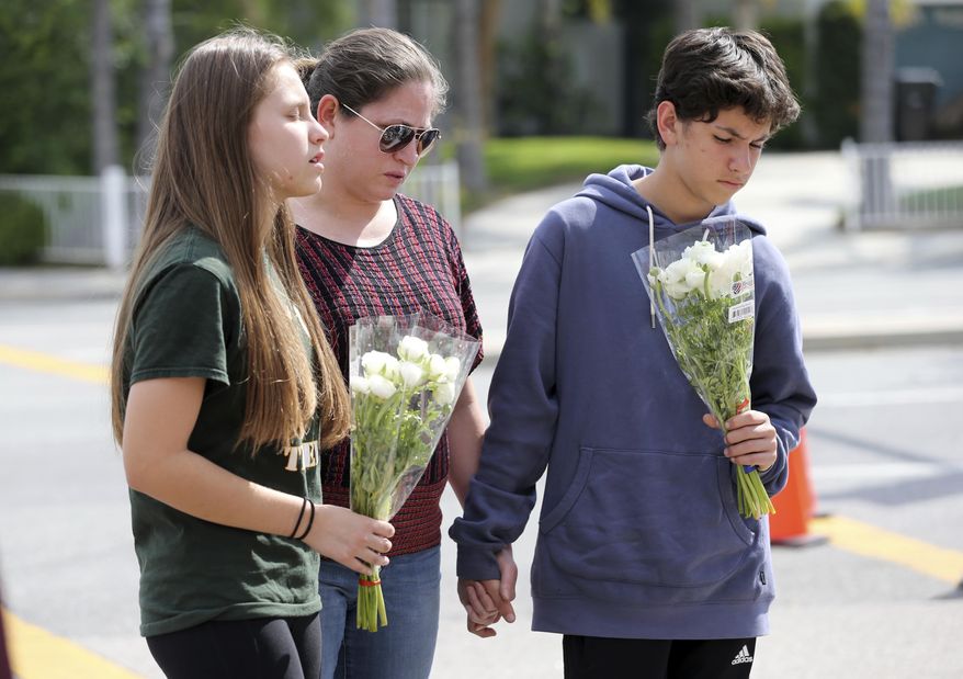 People pray before placing flowers at a sidewalk memorial to the teacher and student who were shot to death Monday at North Park Elementary School in San Bernardino, Calif., Tuesday, April 11, 2017. (AP Photo/Reed Saxon)