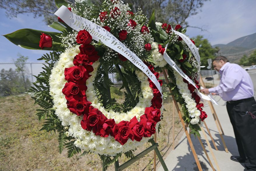 A man places wreathes, including one from President Donald Trump, left, at a sidewalk memorial to the teacher and student who were shot to death at North Park Elementary School in San Bernardino, Calif., Tuesday, April 11, 2017. (AP Photo/Reed Saxon)
