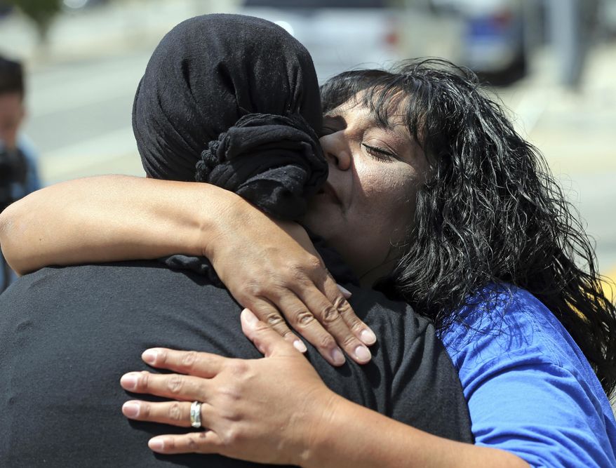 After leading a prayer group, Marie Cabrera, right, embraces one of the group members near a sidewalk memorial dedicated to the teacher and student who were shot to death Monday at North Park Elementary School in San Bernardino, Calif., Tuesday, April 11, 2017. (AP Photo/Reed Saxon)