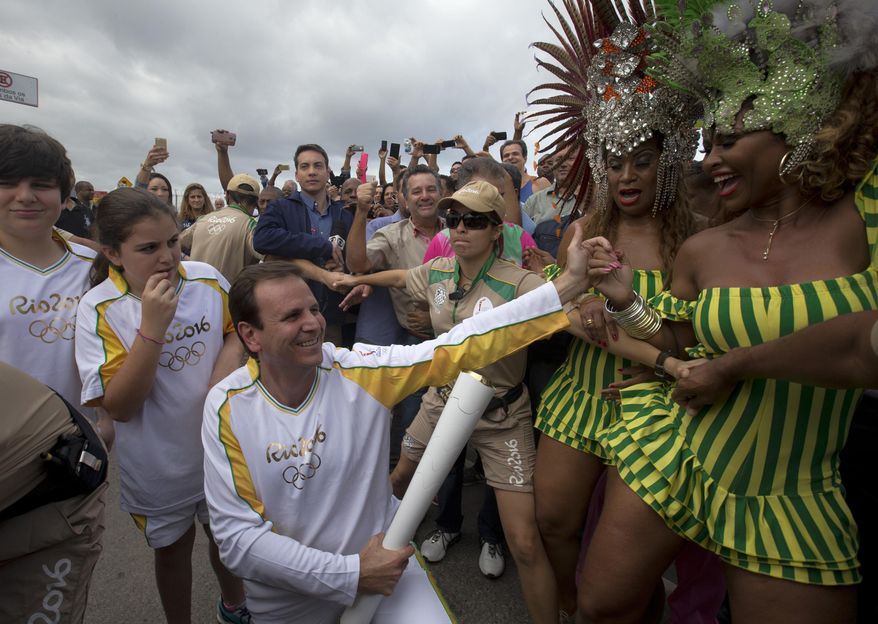 File - In this Aug. 3, 2016 file photo, Rio de Janeiro's Mayor Eduardo Paes, center, holds the Olympic torch, while members of the Mangueira samba school dance, in Rio de Janeiro, Brazil. The former Rio de Janeiro Mayor, the moving force behind organizing last year's Olympics, is being investigated for accepting at least 15 million Brazil reals ($5 million) in payments to facilitate construction projects tied to the Games. (AP Photo/Silvia Izquierdo, File)