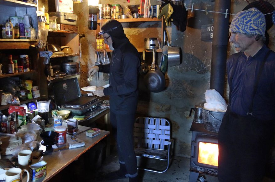 In this photo taken April 1, 2017, Kevin Klinefelter, left, prepares to fry Spam on a griddle as John Dittli, right, looks on as they spend the night in a snow survey cabin near Bishop Pass in the Inyo National Forest near Bishop, Calif. Crews stay out as long as two weeks in alpine wilderness, battling the elements, skirting avalanche terrain and plodding through deep powder to gather the data, a practice that has endured even as new technology tries to gauge the state's expected water supply from snowmelt. (AP Photo/Brian Melley)