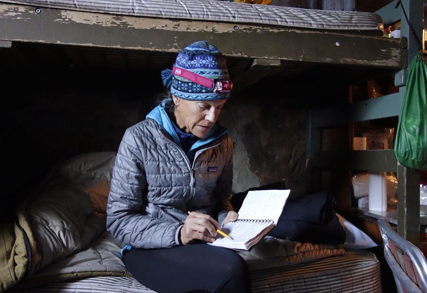 In this photo taken April 1, 2017, Ann Klinefelter reviews log book entries of past snow measurements inside a snow survey cabin near Bishop Pass in the Inyo National Forest near Bishop, Calif. Crews stay out as long as two weeks in alpine wilderness, battling the elements, skirting avalanche terrain and plodding through deep powder to gather the data, a practice that has endured even as new technology tries to gauge the state's expected water supply from snowmelt. (AP Photo/Brian Melley)