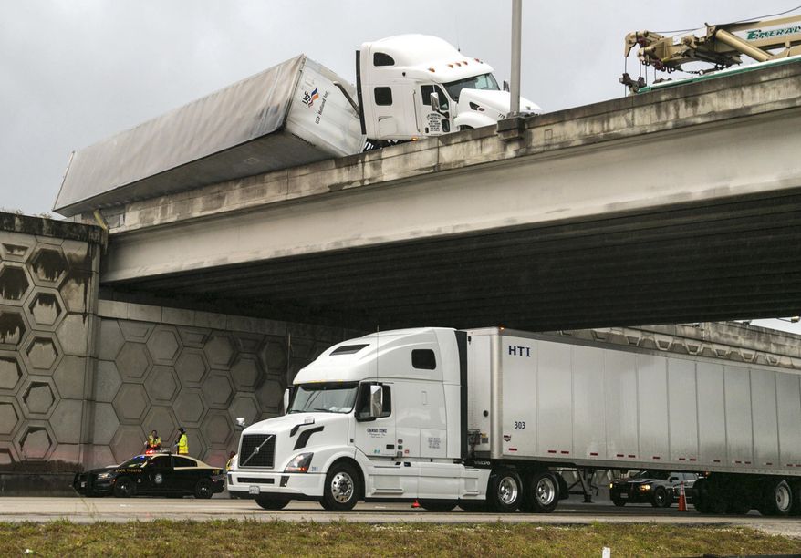 CORRECTS TO TOW TRUCK WORKER, NOT DRIVER - A tractor trailer dangles off the Congress Avenue overpass over I-95 early Wednesday, April 12, 2017, in West Palm Beach, Fla. The Florida Highway Patrol says a tow truck worker fell to his death from an overpass on Interstate 95 while helping to upright an overturned tractor trailer. (Lannis Waters/Palm Beach Post via AP)
