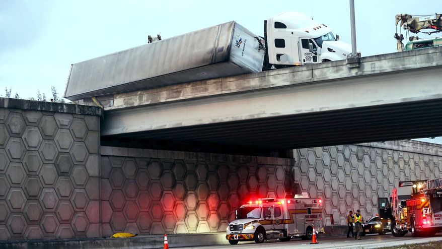 CORRECTS TO TOW TRUCK WORKER, NOT DRIVER - A tractor trailer dangles off the Congress Avenue overpass over I-95 early Wednesday, April 12, 2017, in West Palm Beach, Fla. The Florida Highway Patrol says a tow truck worker fell to his death from an overpass on Interstate 95 while helping to upright an overturned tractor trailer. (Lannis Waters/Palm Beach Post via AP)