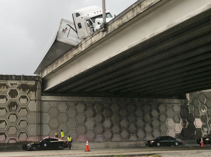 CORRECTS TO TOW TRUCK WORKER, NOT DRIVER - A tractor trailer dangles off the Congress Avenue overpass over I-95 early Wednesday, April 12, 2017, in West Palm Beach, Fla. The Florida Highway Patrol says a tow truck worker fell to his death from an overpass on Interstate 95 while helping to upright an overturned tractor trailer. (Lannis Waters/Palm Beach Post via AP)