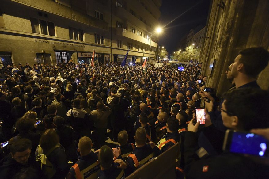 Demonstrators are watched by police as they protest against the amendment of the higher education law that could force a Budapest university founded by billionaire American philanthropist George Soros to close, in front of the Ministry of Human Resources, in Budapest, Sunday, April 9, 2017. Hungarian President Janos Ader said Monday April 10, 2017, in a statement that he has signed the bill setting new conditions for foreign universities in line with the Constitution, and called on the government to “immediately” begin talks with the affected institutions to secure compliance with the new rules.(Zoltan Balogh/MTI via AP)