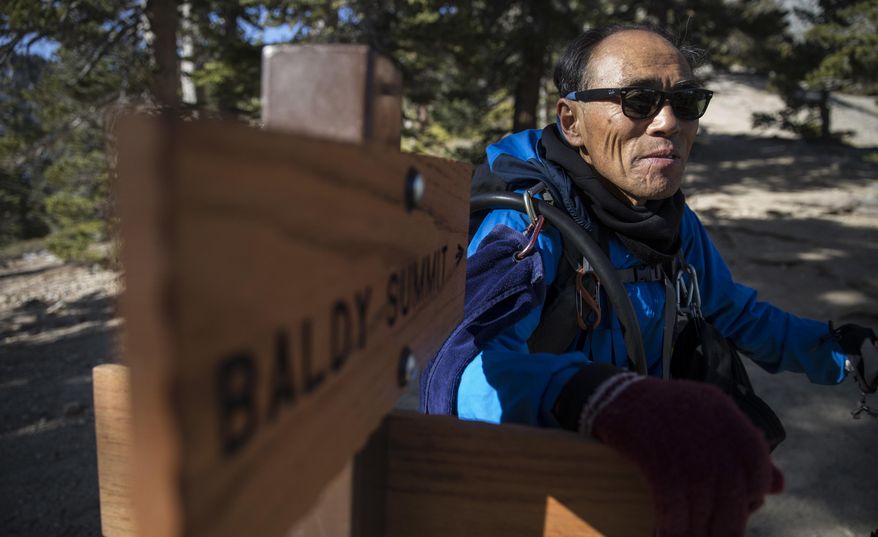 In this Dec. 14, 2016 photo, Seuk “Sam” Kim pauses at a trail sign on approach to Mount Baldy, in Mount Baldy, Calif. A man found dead on Southern California’s towering Mount Baldy was identified Wednesday, April 12, 2017, as the veteran hiker who climbed the famed peak more than 700 times and served as an unofficial mountain ambassador, welcoming other hikers and sharing food with them. (Brian van der Brug /Los Angeles Times via AP)