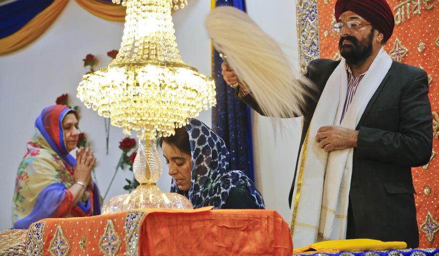 In this April 9, 2017 photo, Balbir Singh Pahwa, right, of the Guru Nanak Darbar Sikh house of worship, shows respect for the holy scripture by waving a fan above Satinder Kaur, center, as she leads a prayer recital at the temple, in Hicksville, N.Y. The beards and turbans are symbols of equality in a religion that opposes India's caste system. (AP Photo/Bebeto Matthews)