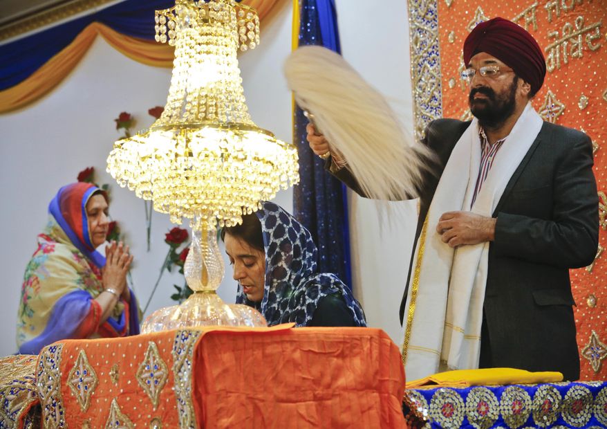 In this April 9, 2017 photo, Balbir Singh Pahwa, right, of the Guru Nanak Darbar Sikh house of worship, shows respect for the holy scripture by waving a fan above Satinder Kaur, center, as she leads a prayer recital at the temple, in Hicksville, N.Y. The beards and turbans are symbols of equality in a religion that opposes India's caste system. (AP Photo/Bebeto Matthews)