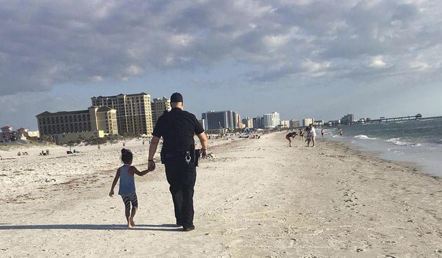 In this April 11, 2017, image provided by Amy Amerell, Clearwater police officer Rich Edmonds holds the hand of a 6-year-old girl on Clearwater Beach, Fla. The girl wandered away from her family and approached another family who called police for assistance. When the child refused to get in the officer's car, he walked her down the beach until they found her family. (Courtesy of Amy Amerell via AP)