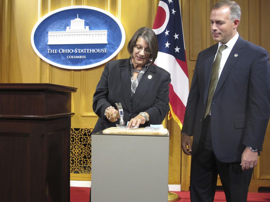 FILE – In this Sept. 17, 2015, file photo, Ohio state Rep. Nickie Antonio, left, D-Lakewood, Ohio, demonstrates tamper resistant pain pills by unsuccessfully trying to pulverize them with a hammer, as state Rep. Robert Sprague, R-Findlay, Ohio, awaits his turn during a news conference at the Statehouse in Columbus, Ohio. Pharmaceutical lobbyists pressed to drive down cost estimates on an Ohio proposal requiring Medicaid and other insurers to cover harder-to-manipulate forms of prescription painkillers known as abuse-deterrent opioids, according to emails obtained by The Associated Press through a public records request. (AP Photo/Andrew Welsh-Huggins, File)