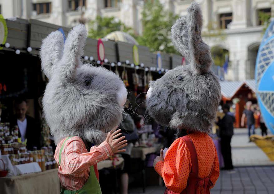 In this Thursday, April 13, 2017, picture entertainers wearing rabbit costumes speak at a fair in Bucharest, Romania. Ahead of Easter, celebrated by both Orthodox and Catholic believers on April 16 processions of priests clad in golden robes carrying foliage on Palm Sunday in a recreation of Jesus' ride into Jerusalem, mixed with more commercial flavored celebrations like an Easter fair outside the giant palace built by late Communist leader Nicolae Ceausescu where entertainers strutted around wearing giant rabbit heads.(AP Photo/Vadim Ghirda)