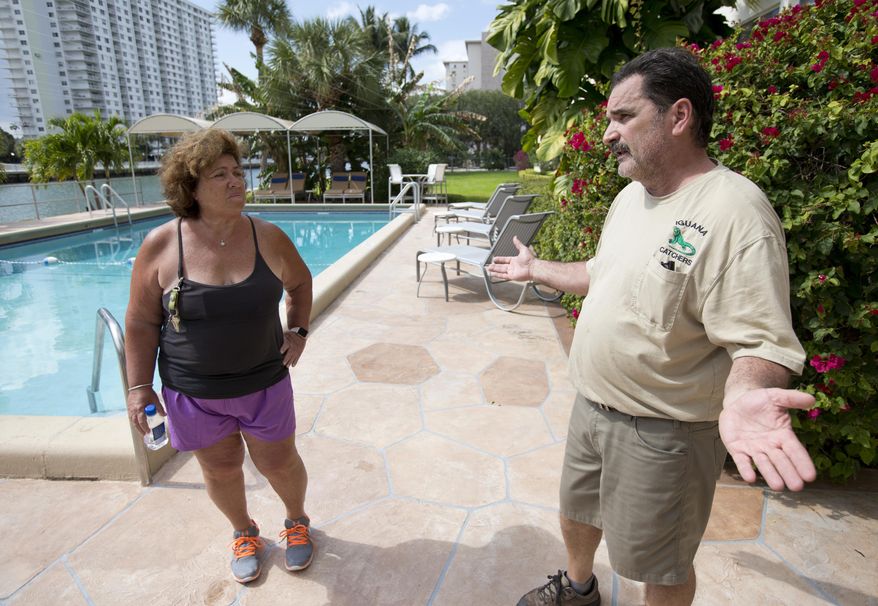 In this Thursday, Feb. 9, 2017 photo, trapper Brian Wood, right, talks with Janet Sarno, board chairwoman at King’s Point Imperial Condo, in Sunny Isles Beach, Fla., about her iguana problem. Sarno hired Wood because the number of iguanas, big adults and bright green babies, hanging around the building’s pool has been growing despite residents’ attempts to chase them away or block their entry. (AP Photo/Wilfredo Lee)