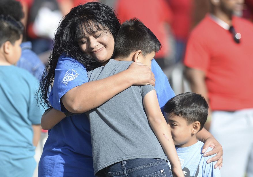 North Park Elementary parent Marie Cabrera of San Bernardino, hugs two students before the start of school Monday, April 17, 2017, at the school in San Bernardino, Calif. Students returned to campus a week after Cedric Anderson, 53, of Riverside, entered the campus with a gun, killing his estranged wife Karen Elaine Smith, 53, student Jonathan Martinez, 8, and wounding student Nolan Brandy, 8, before turning the gun on himself. (John Valenzuela /Los Angeles Daily News via AP)