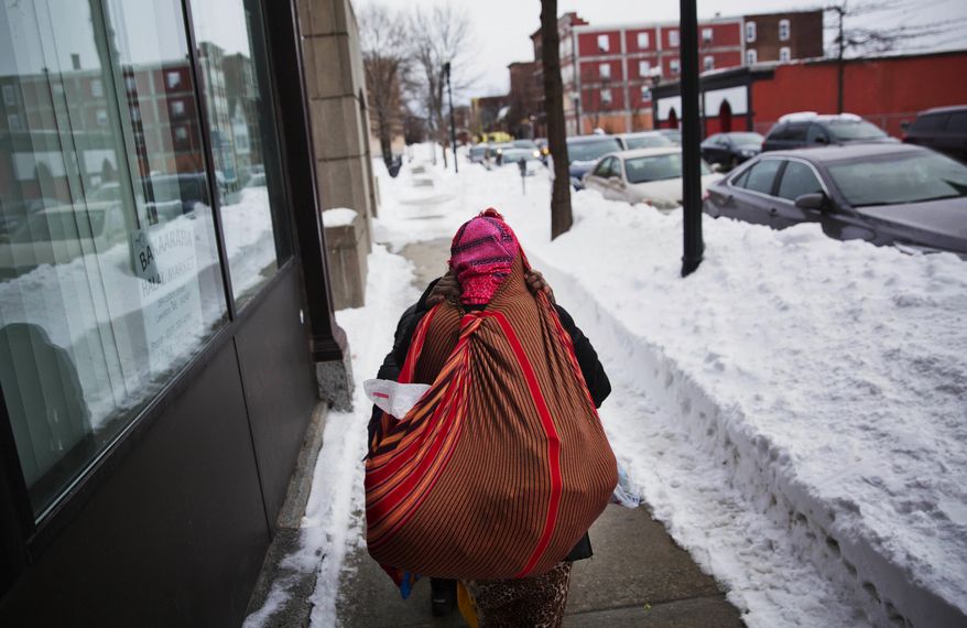 ADVANCE FOR USE WEDNESDAY, APRIL 19, 2017 AND THEREAFTER-A woman carries goods on her back after shopping at one of the many stores downtown owned by African refugees who have settled in Lewiston, Maine, Wednesday, March 15, 2017. Maine offers a welfare program called General Assistance, which provides impoverished people with vouchers for rent, utilities and food. The amount refugees has bounced up and down over the years, but it accounts for less than 1 percent of the budget, said deputy city administrator Phil Nadeau. (AP Photo/David Goldman)