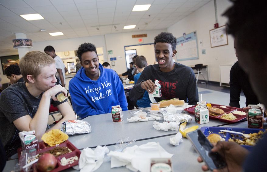 ADVANCE FOR USE WEDNESDAY, APRIL 19, 2017 AND THEREAFTER-Abdiaziz Shaleh, right, a Lewiston high school senior and co-captain of the soccer team, and Essa Gedi, center, both whose families emigrated from Somalia, sit with classmate Isiah Leach, left, during lunch in the school's cafeteria in Lewiston, Maine, Wednesday, March 15, 2017. Two years ago, immigrant children led the high school soccer team to win the state championship, a moment heralded as a triumph for the city's embrace of its immigrant community. (AP Photo/David Goldman)