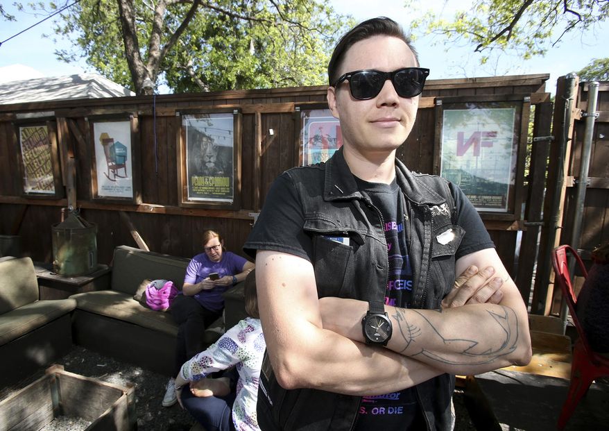In this Friday, April 7, 2017, photo, artist Shay Scranton stands near some of his art work located on the outside walls of the local coffee shop Common Grounds, in Waco, Texas. Scranton not only creates concert posters for bands and fans but has an online store to sell pins and patches. (Jerry Larson/Waco Tribune-Herald via AP)