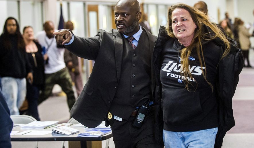 In this Thursday, April 20, 2017, photo, Flint police Officer Kristopher Jones removes resident Leah Palladeno, in handcuffs, from a town hall meeting at House of Prayer Missionary Baptist Church, related to the city's crisis with lead-tainted water, in Flint, Mich. Police say six people were arrested for disorderly conduct or other reasons. The event was held after Flint Mayor Karen Weaver reversed course Tuesday and recommended that Flint continue getting its drinking water from a Detroit-area system long term instead of a new pipeline. (Jake May/The Flint Journal-MLive.com via AP)