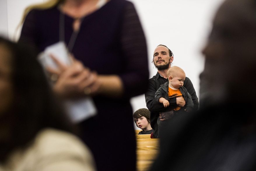 In this Thursday, April 20, 2017, photo, Flint resident Adam Murphy and two of his children listen closely after his wife, Christina, voiced her opinions in ongoing issues with the Flint water crisis during a town hall meeting at House of Prayer Missionary Baptist Church, in Flint, Mich. (Jake May/The Flint Journal-MLive.com via AP)