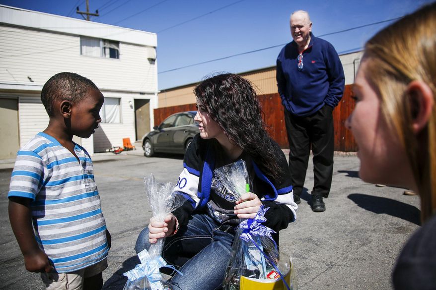 In this Thursday, April 13, 2017 photo, Gunnison Valley High School students Tiandra Taylor, right, and Taneisa Taylor, center, give a boy an easter basket while Don Ward, a retired high school history teacher, looks on in the South Parc Apartments in South Salt Lake, Utah. Ward, estimated that he and others have helped more than 20,000 refugees in Salt Lake County over the past eight years. And he's done so while battling cancer. (Nicole Boliaux/The Deseret News via AP)