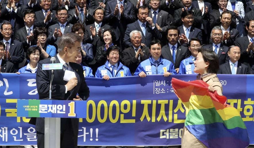 A protester holding a rainbow flag, approaches South Korea's presidential candidate Moon Jae-in from the Democratic Party, left, at National Assembly in Seoul, South Korea, Wednesday, April 26, 2017. South Korean presidential front-runner Moon Jae-in has outraged persecuted sexual minority groups by saying during a television debate that he opposes homosexuality. (Ahn Jung-won/Yonhap via AP)