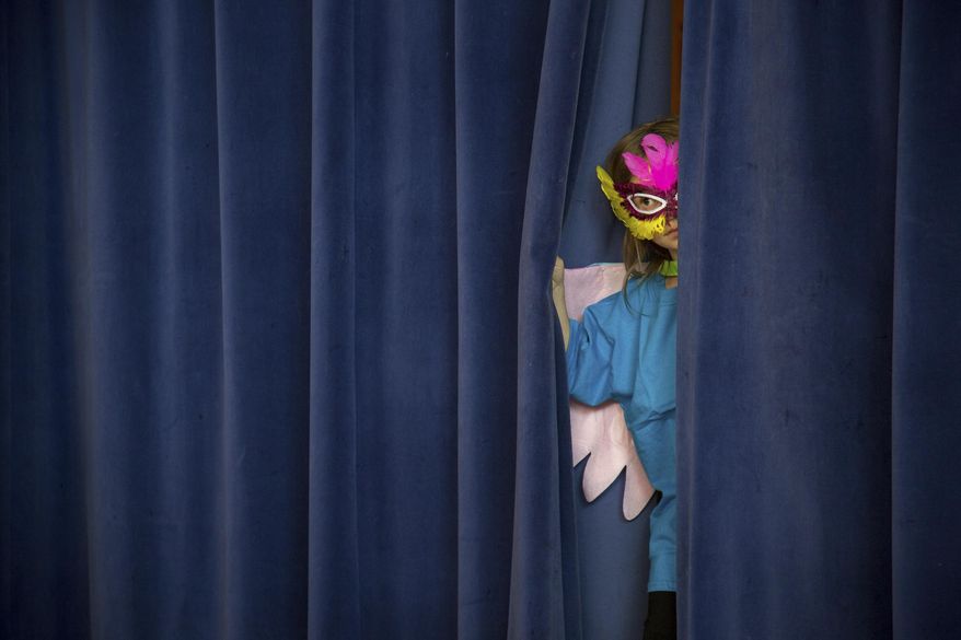 In this Wednesday, April 19, 2017 photo, Jaidyn Brown peaks through the curtain to watch her classmates from backstages at a dress rehearsal of T.O. Smith Elementary School's bilingual Wizard of Oz play, in Ogden, Utah. T. O. Smith is one of two elementary schools in Ogden that offer dual language immersion programs in English and Spanish. (Benjamin Zack /Standard-Examiner via AP)