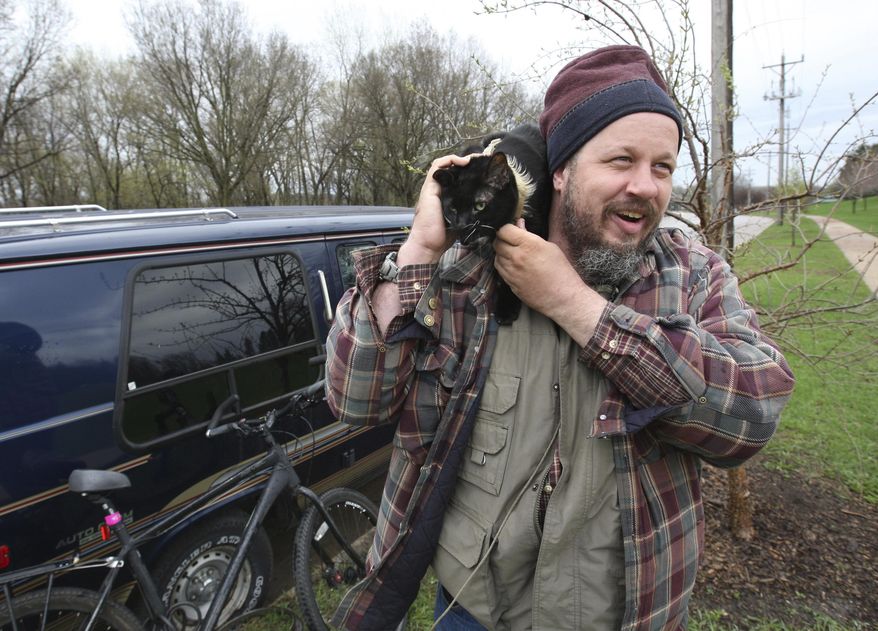 Corey Jacob plays with his cat, Nighty, outside the van he has been sleeping in, Tuesday April 18, 2017 in Rochester, Minn. Pulling together all of his resources, Jacob got the van in March. A drunk driver slammed into the van a few nights ago while it was parked disabling it. (Ken Klotzbach/The Rochester Post-Bulletin via AP)
