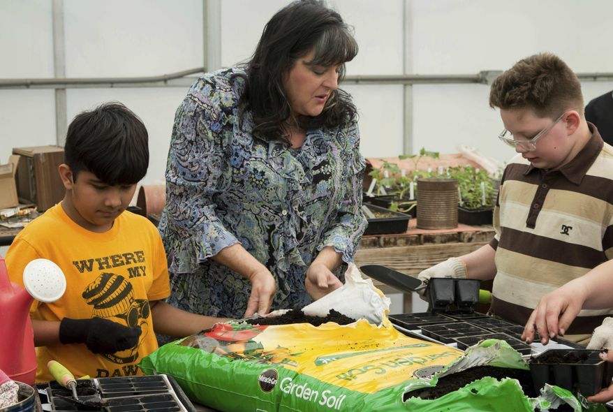 ADVANCE FOR WEEKEND EDITIONS - In this April 13, 2017, photo, Dayton School District after-school program teacher Leslie Sweetwood helps Dhrau Hans, left, and Nova Laws get seedling trays ready for planting inside the Dayton High School's greenhouse in Dayton, Washington. (Dian Ver Valen/Walla Walla Union-Bulletin via AP)