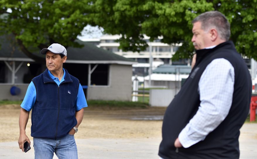 Assistant trainer Baldemar Bahena, left, and trainer Dale Romans look on as a groom bathes a horse at Churchill Downs, Tuesday, April 18, 2017, in Louisville, Ky. Immigrants have become indispensable at Churchill Downs and other tracks. Now, fear is spreading that a Trump administration crackdown on immigration will be a calamity both for the tracks and for many of their workers. (AP Photo/Timothy D. Easley)