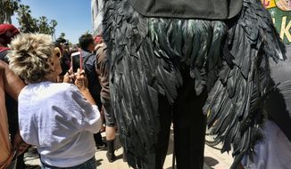 In this Sunday, April 30, 2017 photo a passerby takes photos during a protest at the Venice Beach Freakshow along the strand in the Venice beach section of Los Angeles. The Venice Beach Freakshow possibly performed its last show on Sunday after announcing it is closing due to a leasing dispute. The Freakshow put on a six-hour performance on the boardwalk serving as a protest, farewell and fundraiser. (AP Photo/Richard Vogel)