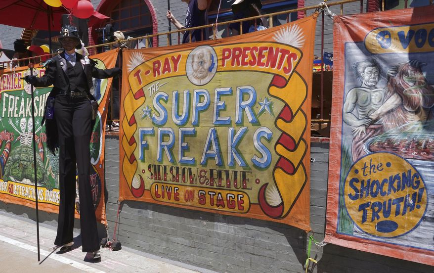 In this Sunday, April 30, 2017 photo, a stilt walker stands by a banner advertising the Venice Beach Freakshow along the strand in the Venice beach section of Los Angeles. The Venice Beach Freakshow possibly performed its last show on Sunday after announcing it is closing due to a leasing dispute. The Freakshow put on a six-hour performance on the boardwalk serving as a protest, farewell and fundraiser. (AP Photo/Richard Vogel)