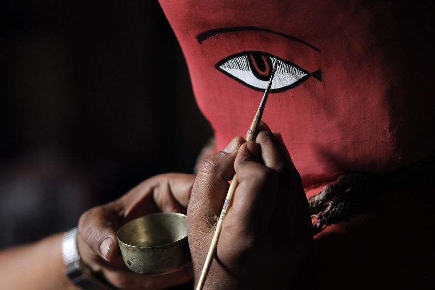 In this April 23, 2017, photo, a Chitrakar artist paints details on the statue of Rato Machindranath in Machindra Bahal in Lalitpur, Nepal. The wide-eyed statue of Machindranath, made from red-painted clay and covered with gold ornaments, is kept under lock and key for months until it is brought out for the Rato Machindranath festival. The harvest festival, which preludes the monsoon season in Nepal, centers on a five-story high chariot that carries the deity in the capital Kathmandu. (AP Photo/Niranjan Shrestha)