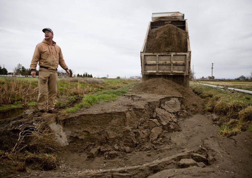 ADVANCE FOR WEEKEND EDITIONS - In this March 30, 2017, photo, Minidoka Irrigation District equipment operator Evan Overson guides a dump truck full of dirt as he prepares to fill a hole in a washed-out access road March 30 along the main drain ditch on Rupert's Meridian Road in Rupert, Idaho. (Pat Sutphin/The Times-News via AP)