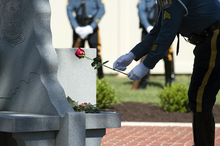 A Delaware State Trooper places a rose for a fallen trooper during the annual wreath-laying ceremony at the Trooper&#x27;s Memorial Wednesday, May 3, 2017, in Dover, Del. Cpl. Stephen Ballard, a state trooper who was fatally shot last week, was honored Wednesday at the ceremony for Delaware State Police officers who have died in the line of duty. (Jason Minto/The Wilmington News-Journal via AP)