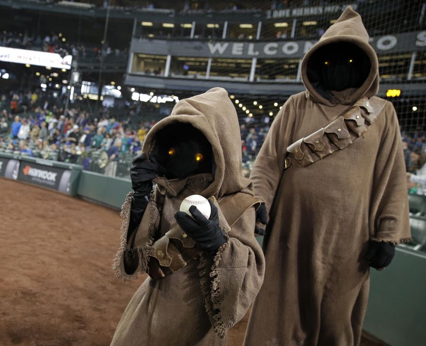 A child dressed as a Jawa Star Wars character carries a baseball before delivering it to the mound before a baseball game between the Seattle Mariners and the Los Angeles Angels, Thursday, May 4, 2017, in Seattle. The appearance was part of a Star Wars Day promotion. (AP Photo/Ted S. Warren)
