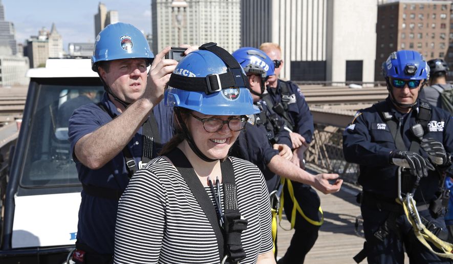 In this Tuesday, May 2, 2017 photo, Associated Press video journalist Ted Shaffrey, left, attaches a miniature camera to a helmet worn by Associated Press reporter Colleen Long, center, before the pair climbed the Brooklyn Bridge with an AP photographer and New York Police Department's elite officers who execute the most difficult rescues, including those on bridges and skyscrapers, in New York. The police officers demonstrated their high-rise rescue skills for the three AP journalists in an exclusive outing scaling the bridge's suspension cables. (AP Photo/Seth Wenig)