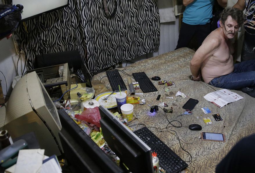 In this April 20, 2017, photo, suspected child webcam cybersex operator, David Timothy Deakin, from Peoria, Ill., with his hands tied behind his back during a raid by investigators, sits on his bed where he handles online sharing of videos of children engaging in sexual acts in Mabalacat, Philippines. Deakin's arrest reveals one of the darkest corners of the internet, where pedophiles in the U.S., Canada, Europe and Australia pay facilitators on the other side of the world to sexually abuse children, directing their moves through online livestreaming services. (AP Photo/Aaron Favila)