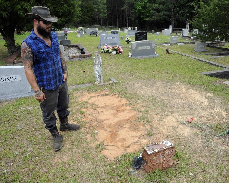 In this photo Wednesday, May 3, 2017 photo, Tyler Goodson of the hit podcast "S-Town" stands at the grave of friend John B. McLemore, who is also featured in the serialized show. Dimes, rocks and trinkets have started showing up on McLemore's headstone since the podcast debuted. But residents of the rural area depicted in the show are uneasy with their community being portrayed as a lousy place best described with an expletive. (AP Photo/Jay Reeves)