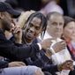 FILE - In this April 5, 2017, file photo, rap artist Travis Scott, center, reacts during an NBA basketball game between the Houston Rockets and Denver Nuggets in Houston. Scott and the Rockets will have a special treat for fans attending Game 6 of the Western Conference semifinals on Thursday night May 11. Everyone will receive exclusive t-shirts designed as part of a collaboration between the Houston rapper and the team. (AP Photo/Michael Wyke, File)