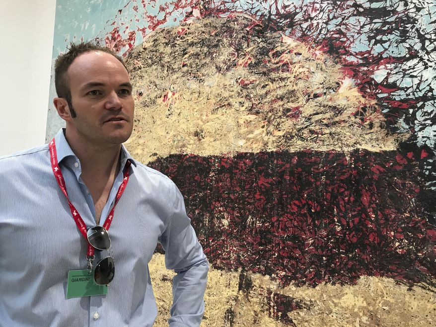 In this photo taken in Venice, Italy, Wednesday, May 10, 2017, US pavilion curator Christopher Bedford stands in front of artist Mark Bradford's 2016 canvas " Go Tell It on the Mountain," part of his show titled ''Tomorrow is Another Day''. (AP Photo/Colleen Barry)