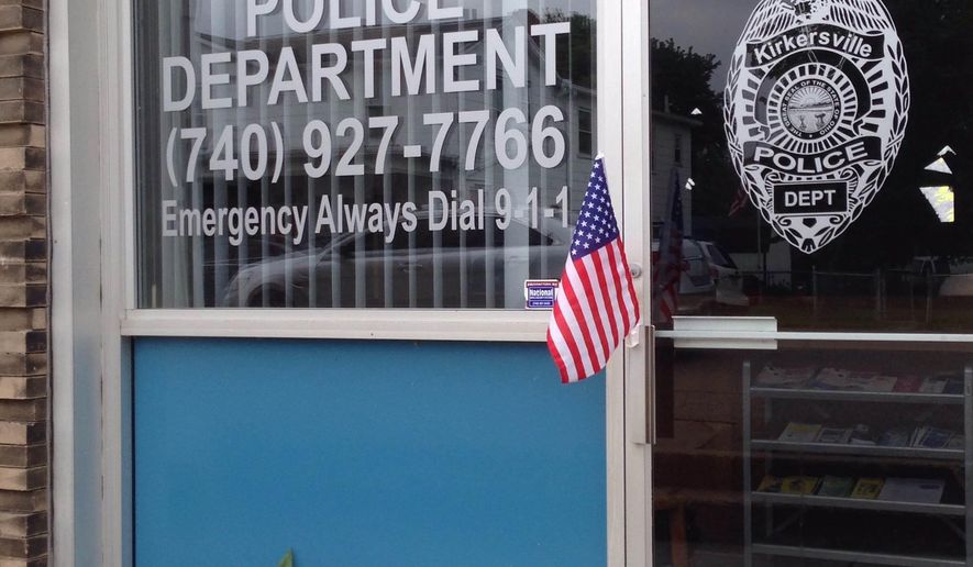 An impromptu memorial of flowers and flags appeared outside the Kirkersville Police Department, on Friday, May, 12, 2017, in Kirkersville, Ohio, after its new chief was shot by an armed gunman. Two workers at nearby Pine Kirk Care Center also were killed. The gunman was found dead inside the center. (AP Photo/Julie Carr Smyth)