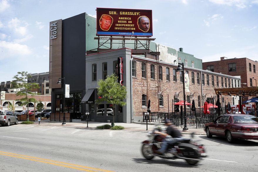 A motorcyclist passes under a billboard on Court Street, Monday, May 15, 2017, in downtown Des Moines, Iowa. The digital billboard just around the corner from U.S. Sen. Chuck Grassley's regional office in Des Moines on Monday began displaying a request for the Senate Judiciary chairman. Between images of President Donald Trump and Vladimir Putin, the message reads, "Sen. Grassley: America needs an independent investigation." (AP Photo/Charlie Neibergall)