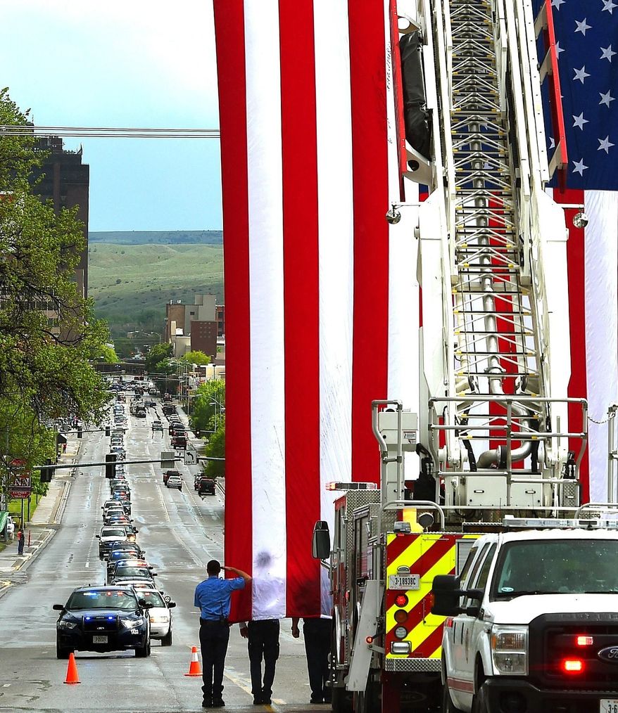The Billings Fire Department raises a flag over North 27th Street as a procession of law enforcement vehicle escorts the body of slain sheriff's deputy Mason Moore to St. Vincent Healthcare, Tuesday, May 16, 2017 in Billings, Mont. Moore, a sheriff's deputy was killed early Tuesday in a shootout that prompted a middle-of-the-night pursuit that spanned more than 100 miles (161 kilometers) across southwestern Montana, involving several law enforcement agencies. (Larry Mayer/The Billings Gazette via AP)