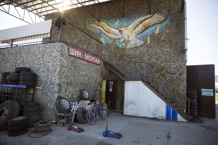 In this photo taken on Wednesday, May 3, 2017, an eagle sculpted and painted by Korshunov is seen above the tire service and restaurant next to a road in Shatura, about 125 kilometers (77,67 miles) east of Moscow, Russia. The playground slide in the background was also built by Mikhail Korhunov. In this sparsely populated village east of Moscow, Mikhail Korshunov's house is visible from far away. Portraits of Russian rulers - from 13th century Novgorod prince Alexander Nevsky to President Vladimir Putin - adorn its facade. (AP Photo/Pavel Golovkin)