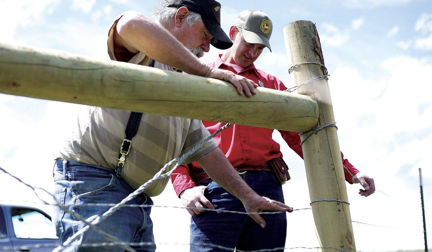 01_Karl Lankford tests the tension of his new wildlife-friendly fence on May 15, 2017 as Wyoming Game and Fish Senior Game Warden Bill Brinegar talks with him about how the new fence will reduce the number of elk, deer and antelope affected by the cow pasture barrier at the base of Sheep Mountain outside of Laramie, Wyo. (Ike Fredregill/Laramie Daily Boomerang via AP)