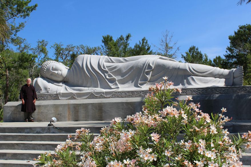 ADVANCE FOR USE SATURDAY, MAY 20 - In this May 16, 2017 photo, Ron Henderson, a staff member at the White Sands Buddhist Center, poses in Mims, Fla., stands next to the Nirvana Buddha statue. The statue is one of three massive monuments currently at the center, and weighs about 40 tons. (Jessica Saggio/Florida Today via AP)
