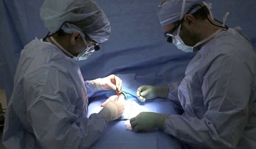 ADVANCE FOR USE MONDAY, MAY 22 - In this May 1, 2017 photo, Dr. Abhishek Julka, left, and Dr. Walker Flannery perform carpal tunnel surgery on Mikaela Rueter as she remains awake at UW Health's American Center Clinic in Madison, Wis. Julka prefers having patients stay alert during the procedure so they can tell him if his instruments hit a nerve. "Particularly for people with small wrists, I really want them awake," he said. (John Hart/Wisconsin State Journal via AP)