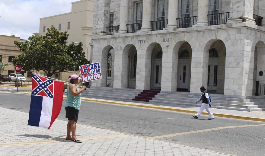 In this May 18, 2017 photograph, Carol Mize holds a Mississippi flag and a sign as she protests outside City Hall in Biloxi, Miss., against Mayor Andrew "FoFo" Gilich's decision to remove the state flag from display at city buildings because it contains the Confederate battle emblem. (AP Photo /Emily Wagster Pettus)